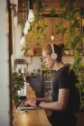 Человек слушает музыку на наушниках во время использования ноутбука в кафе — стоковое фото