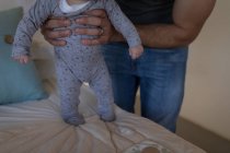 Mid section of father holding baby boy on bed at home. — Stock Photo