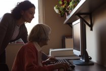 Cuidador auxiliando a mulher idosa enquanto trabalhava no computador na sala de enfermagem — Fotografia de Stock