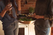 Sección media de amigos tomando vino mientras preparan comida en la cocina - foto de stock