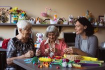 Zwei Seniorinnen basteln mit Hausmeister im Pflegeheim künstliche Blume — Stockfoto
