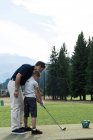 Father assisting his son to play golf in the course — Stock Photo
