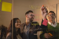 Smiling business people discussing ideas on glass wall and sticky notes at office. — Stock Photo