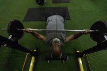 Vista de ángulo alto del hombre mayor haciendo ejercicio con barra de pesas en el gimnasio . - foto de stock