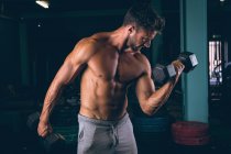 Мускулистый мужчина тренируется с гантелями в фитнес-студии — стоковое фото