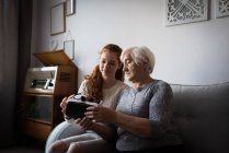 Nieta ayudando a la abuela con auriculares de realidad virtual en casa - foto de stock