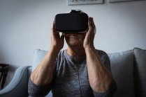 Пожилая женщина использует гарнитуру виртуальной реальности в гостиной дома — стоковое фото