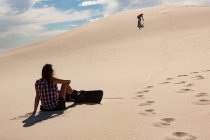 Mujer mirando al hombre haciendo sandboard en el desierto en un día soleado - foto de stock