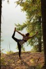 Вмістити жінку, що виконує розтягування в пишному зеленому лісі під час світанку — стокове фото