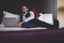 Empresário usando laptop na cama no hotel — Fotografia de Stock