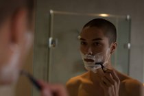 Joven afeitándose la barba en el baño - foto de stock