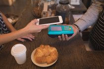 Cliente haciendo un pago móvil en el mostrador en la cafetería - foto de stock