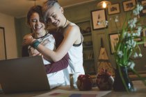 Happy lesbian couple embracing while using laptop at home. — Stock Photo