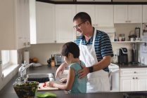 Aufmerksamer Vater hilft seinem Sohn beim Gemüseschneiden in der Küche — Stockfoto