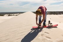 Homem usando sandboard na duna de areia no dia ensolarado — Fotografia de Stock