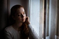 Ragazza adolescente riflessivo guardando attraverso la finestra a casa — Foto stock