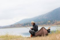 Homme assis sur un bateau à l'extérieur de la rivière avec son équipement de pêche — Photo de stock