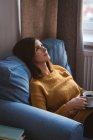Junge Frau entspannt sich tagsüber zu Hause auf dem Sofa mit einer Tasse Kaffee — Stockfoto