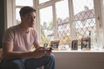 Man playing video game in living room by window with grid. — Stock Photo
