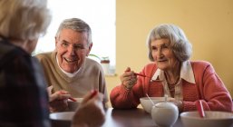 Sorrindo amigos seniores interagindo enquanto toma café da manhã em casa de repouso — Fotografia de Stock