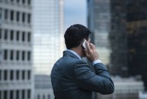 Вид ззаду бізнесмена, що розмовляє на мобільному телефоні проти хмарочоса — стокове фото