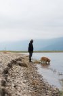 Hombre dejando a su perro mascota beber agua de la orilla del río - foto de stock