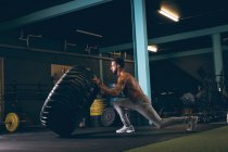 Uomo muscolare che si allena con pneumatici pesanti nella palestra — Foto stock
