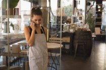 Улыбающаяся официантка разговаривает по мобильному телефону в кафе — стоковое фото