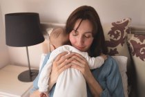 Joven mamá sosteniendo y abrazando a su bebé en casa - foto de stock