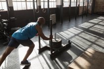 Homem sênior determinado empurrando trenó de peso no estúdio de fitness . — Fotografia de Stock