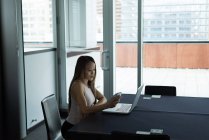 Азіатський бізнес-леді сидячи самі працюють на ноутбуці, використовуючи її мобільний в офісі — стокове фото