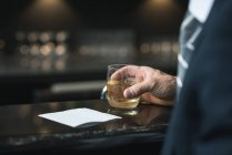 Imagem cortada de homem de negócios com copo de uísque no balcão do hotel — Fotografia de Stock