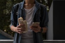 Junger Mann benutzt Handy beim Burgeressen im Treppenhaus — Stockfoto