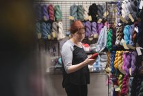 Жінка дивиться на пряжу під час використання цифрового планшета в кравецькому магазині — стокове фото