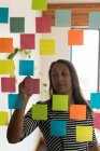 Female executive writing on sticky notes in office — Stock Photo
