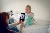 Mother taking photo of her baby girl with mobile phone at home — Stock Photo