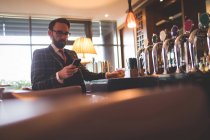 Geschäftsmann benutzt Handy, während er Whiskey in Bar trinkt — Stockfoto