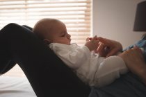 Jeune mère assise sur le lit tenant bébé sur les genoux et jouant à la maison — Photo de stock