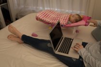 Mãe usando laptop enquanto bebê menino dormindo na cama em casa . — Fotografia de Stock