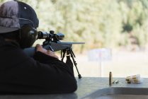 Visão traseira do homem apontando rifle sniper no alvo no alcance de tiro — Fotografia de Stock