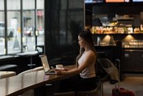 Empresária segurando telefone celular enquanto trabalhava no laptop no refeitório — Fotografia de Stock