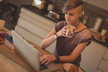 Женщина пьет кофе дома, пользуясь ноутбуком . — стоковое фото