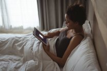Frau benutzt digitales Tablet auf Bett im Schlafzimmer — Stockfoto