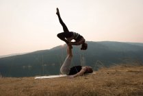 Pareja deportiva practicando acro yoga en un exuberante terreno verde en el momento de dwan - foto de stock