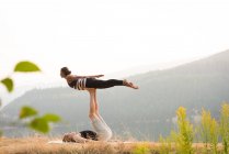 Спортивна пара практикує акро-йогу в пишному зеленому ґрунті під час дван — стокове фото