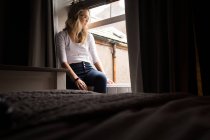 Молодая женщина сидит на окне в спальне — стоковое фото