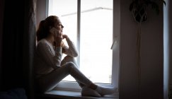 Teenager-Mädchen sitzt auf Fensterbank und telefoniert zu Hause — Stockfoto