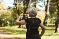 Senior mulher usando um relógio inteligente em um parque em um dia ensolarado — Fotografia de Stock