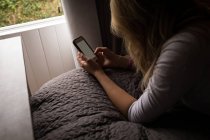 Mujer joven usando su teléfono móvil tumbado en la cama en el dormitorio - foto de stock