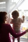 Madre con su bebé mirando a través de la ventana en casa - foto de stock